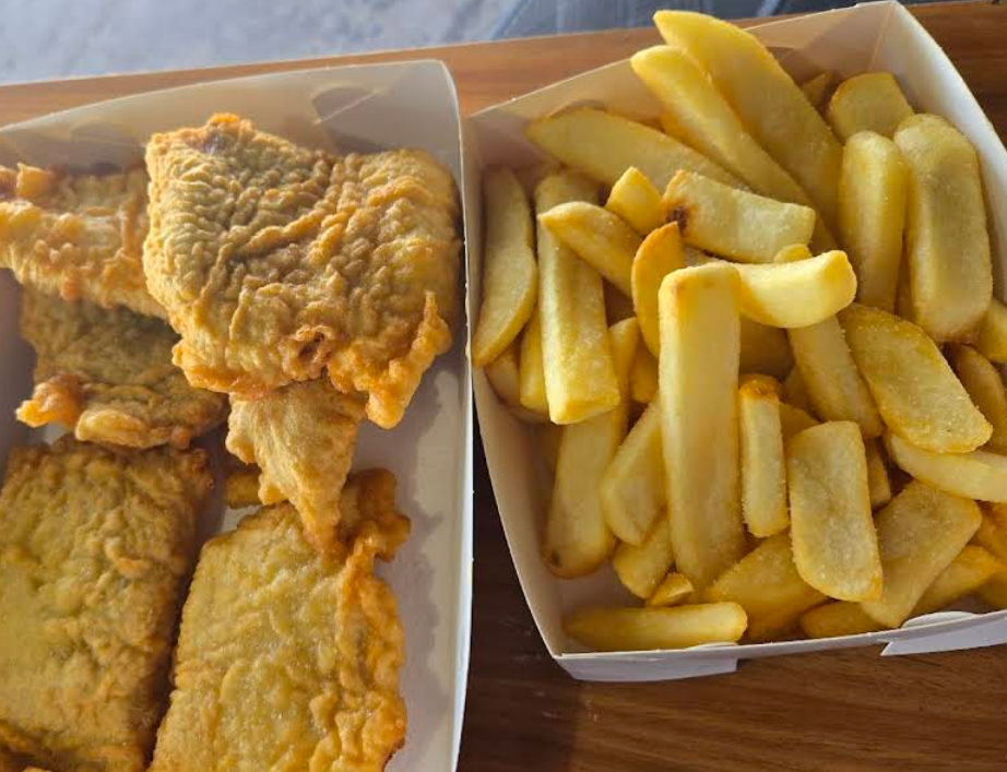Battered fish fillets beside a box of thick cut chips