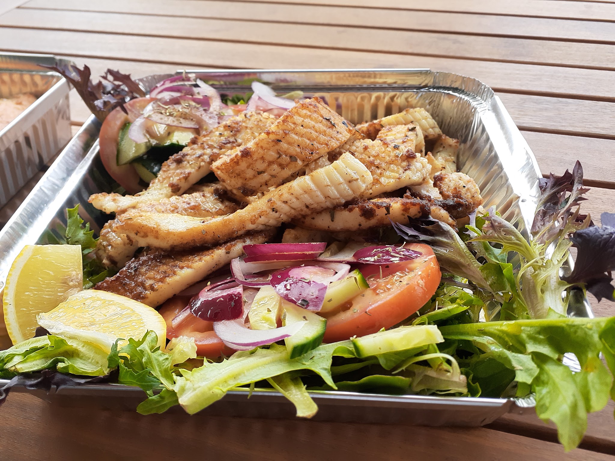 Grilled fish fillets on a garden salad with lemon wedges