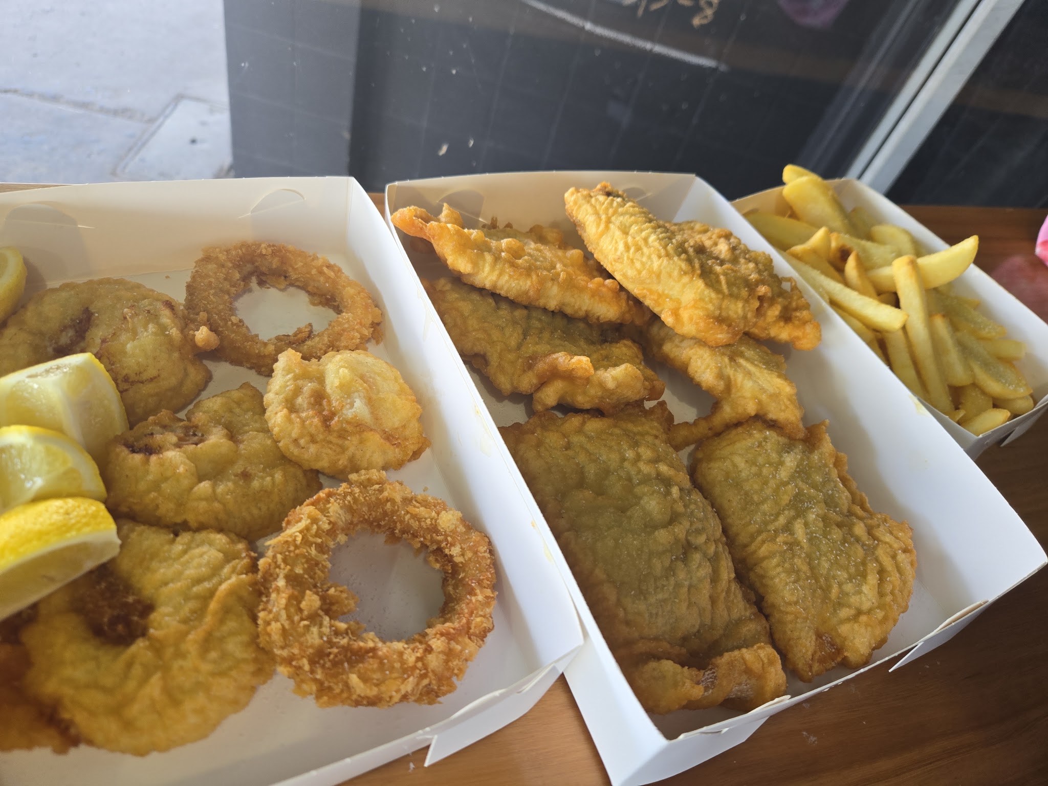 Battered fish, calamari rings and chips in open takeaway boxes