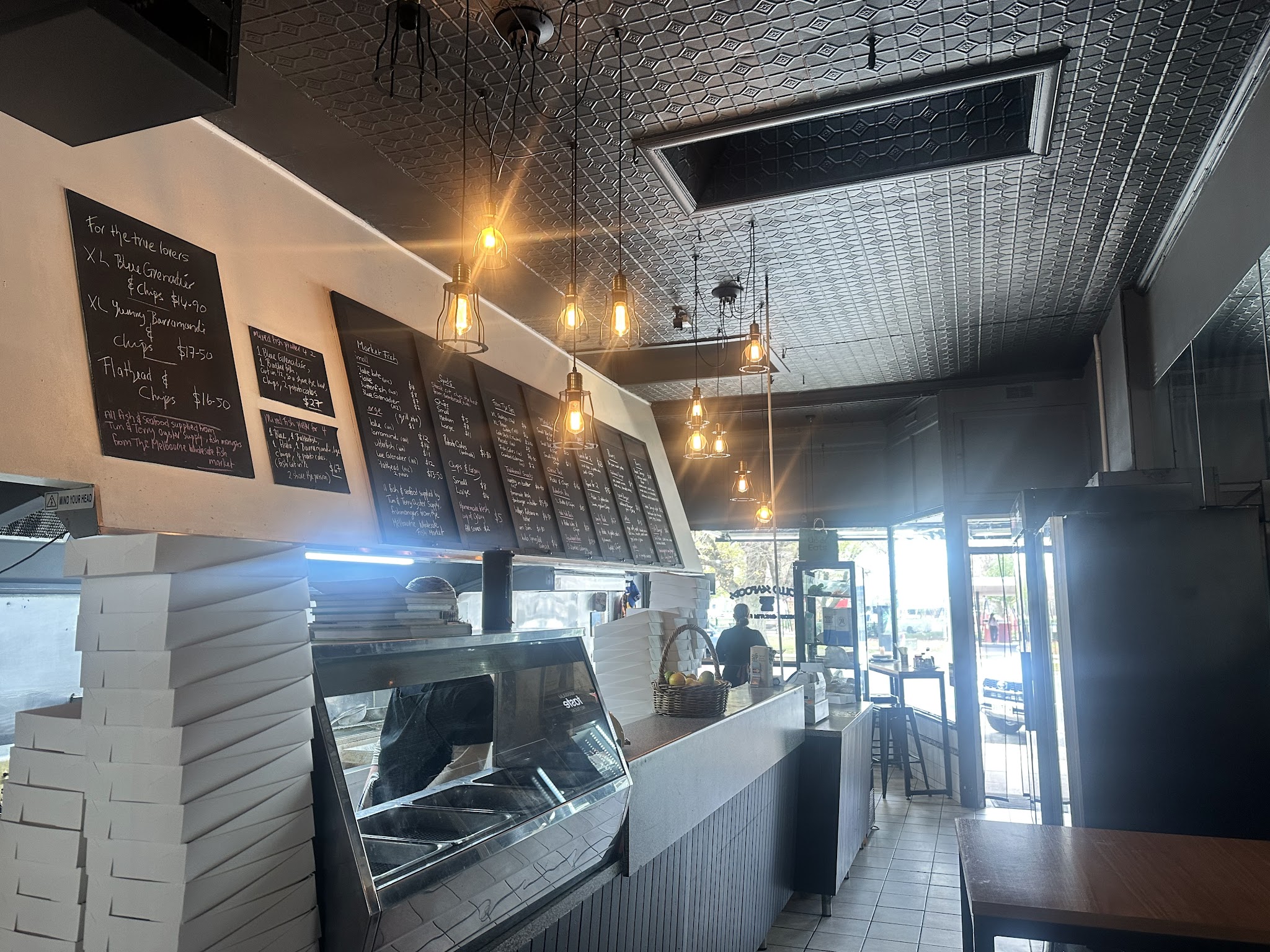 Inside the shop, looking along the counter to the handwritten chalkboard menus under a pressed tin ceiling