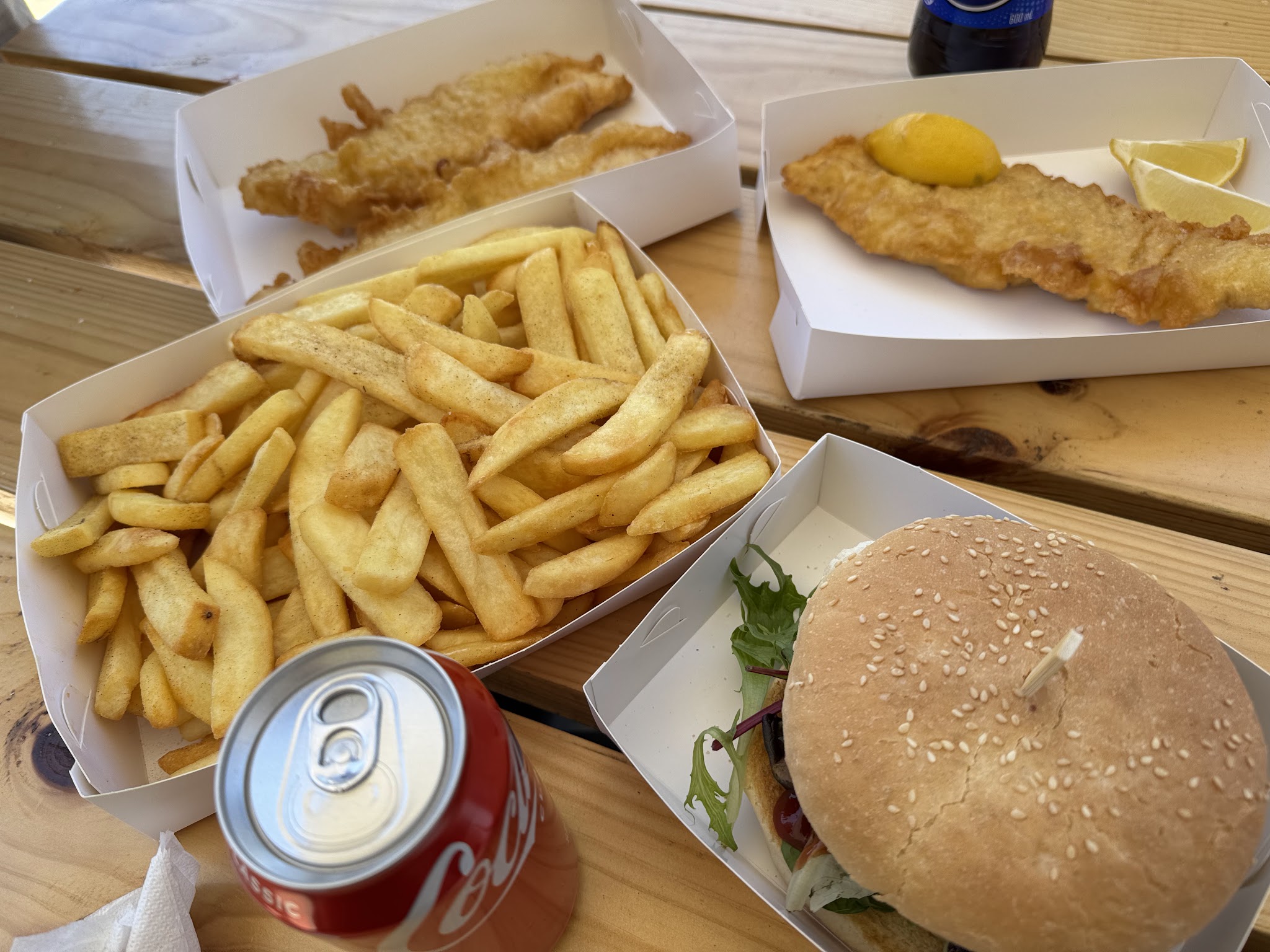 Fish, a large box of chips and a burger on a timber picnic bench